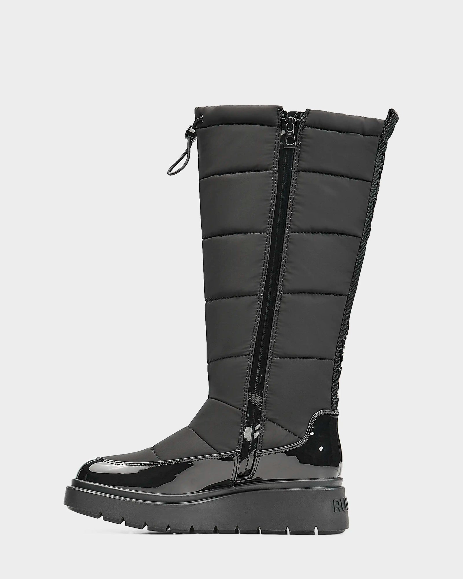 The Rudsak CLAUDE - L223506 Black women's tall quilted winter boot features a shiny patent toe and heel, quilted upper, side zipper, ridged sole, and top drawstring. This waterproof boot is stylish, warm, and comfortable.
