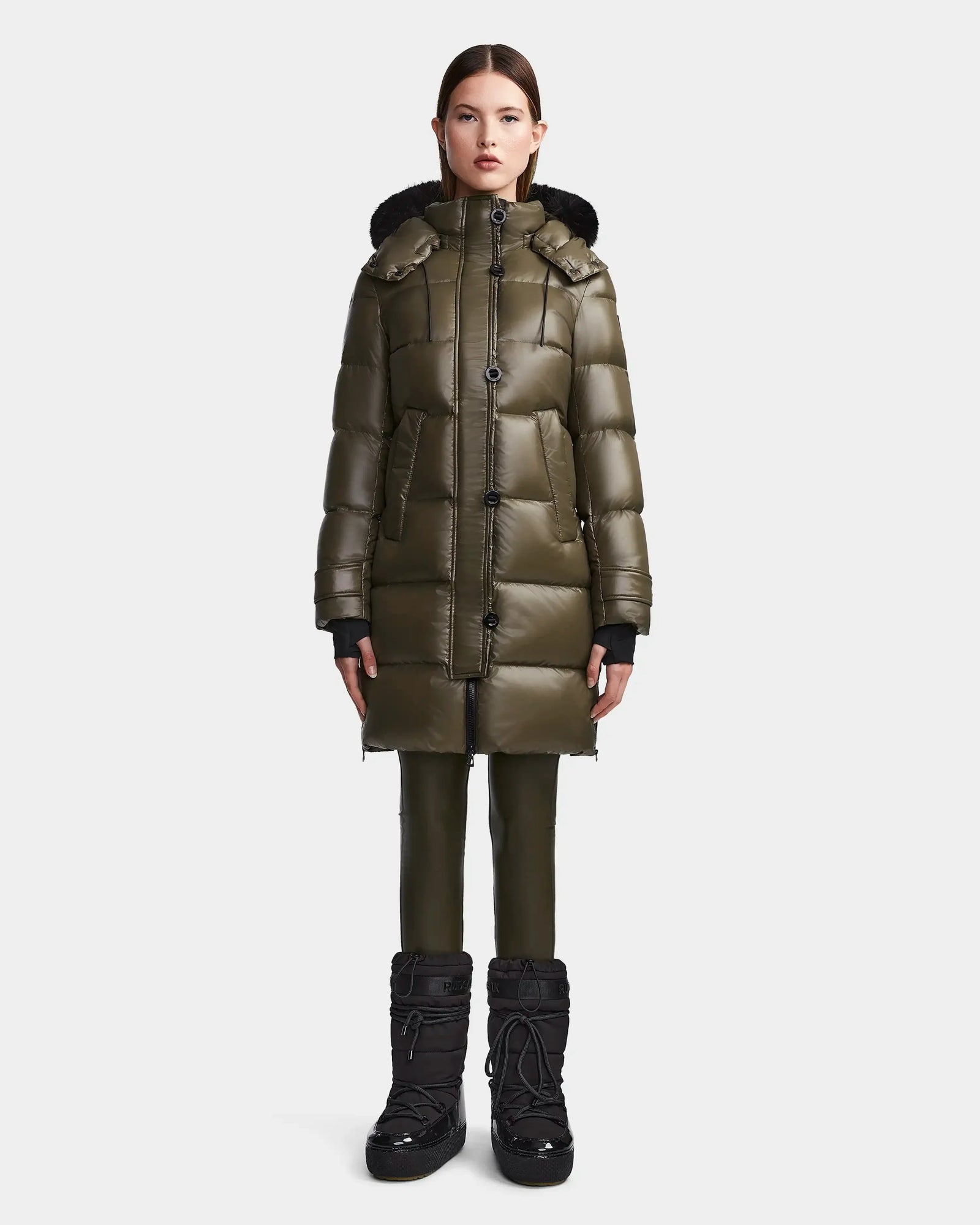 A woman stands facing forward wearing the Rudsak MEYA S - L123521 Light Olive women's down puffer coat, styled with matching green pants and black winter boots against a plain white background.