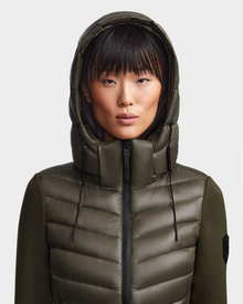A woman with straight black hair and bangs wears the Rudsak MALYA - L121006 Light Olive down jacket, zipped up, standing against a plain light background and looking directly at the camera.