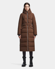 A woman stands facing forward against a plain white background wearing the RUDSAK CALI - 8122502 COHIBA long brown belted down puffer coat with hood and front zipper, paired with black lace-up boots.