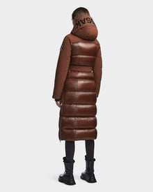 A person faces away, wearing the RUDSAK CALI - 8122502 COHIBA womens long brown winter coat with a hood featuring bold black letters, paired with black leggings and chunky boots against a white background.