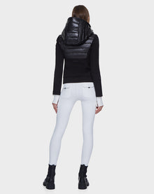 A person stands facing away, wearing the Rudsak MABS - 8121012 BLACK lightweight activewear jacket with a shiny puffer hood, paired with white fitted pants and black ankle boots against a plain white background.