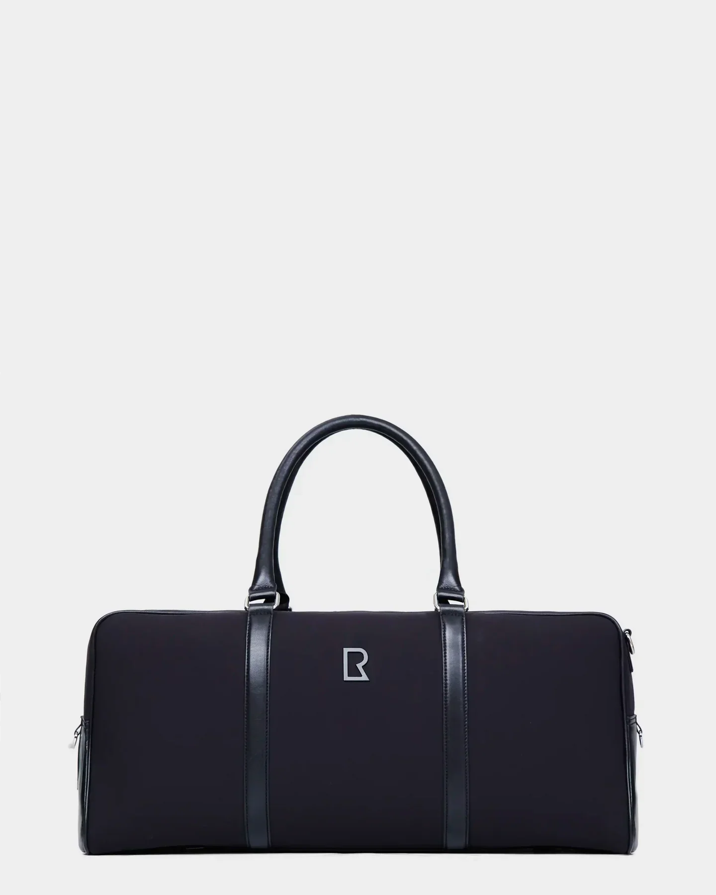 The Rudsak OLIVER - 9323507 Black is a unisex duffel bag with dual handles, vertical leather-like accents, and a central silver geometric logo, offering a luxurious travel look against a plain light background.